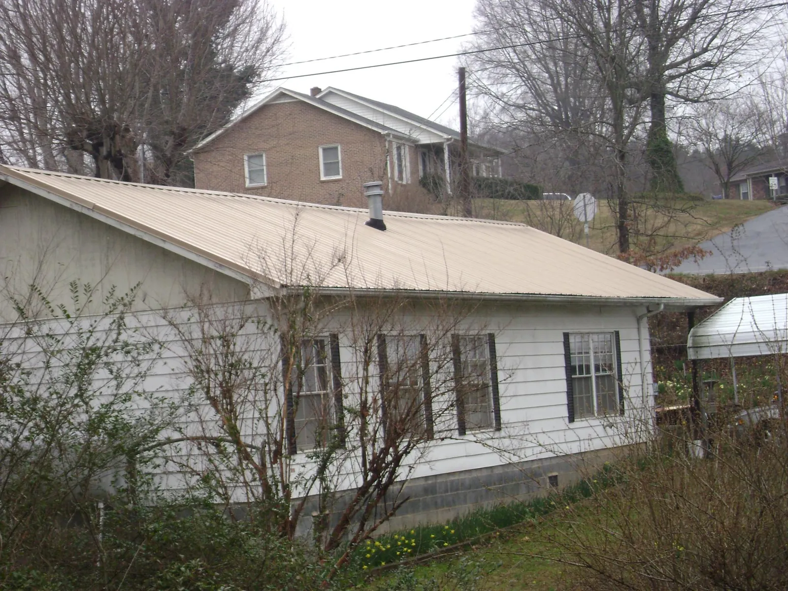 Tan metal roof on a white sided house set into a hillside — Commercial Roofing by Roofing Brothers in Maysville
